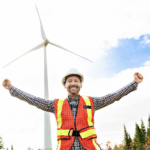 wind turbine technician celebrating first job. turbine in the background.