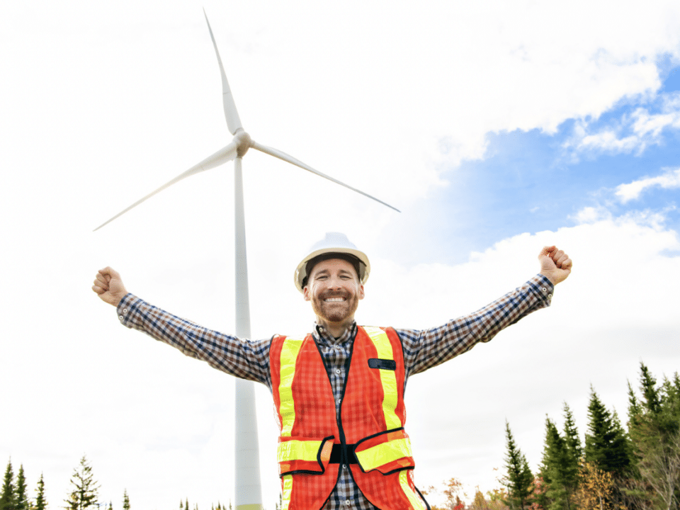 wind turbine technician celebrating first job. turbine in the background.