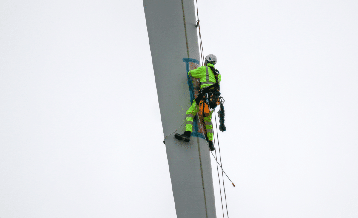 Blade repair being performed on wind turbine blade in harness in the air by worker