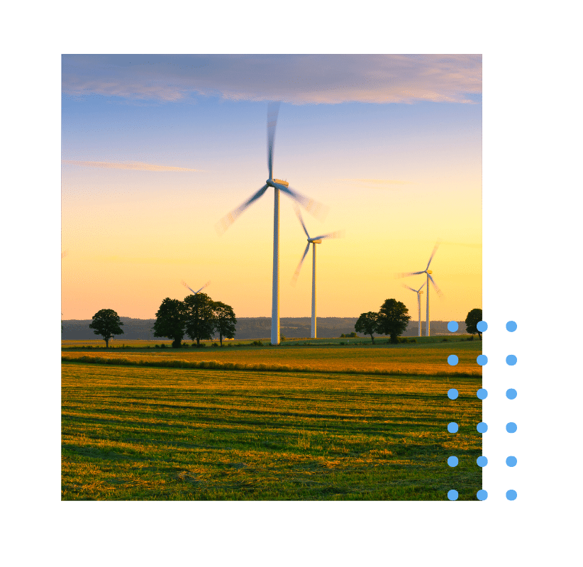 Wind turbines rotating at sunset in a wide-open agricultural field with trees scattered across the landscape.