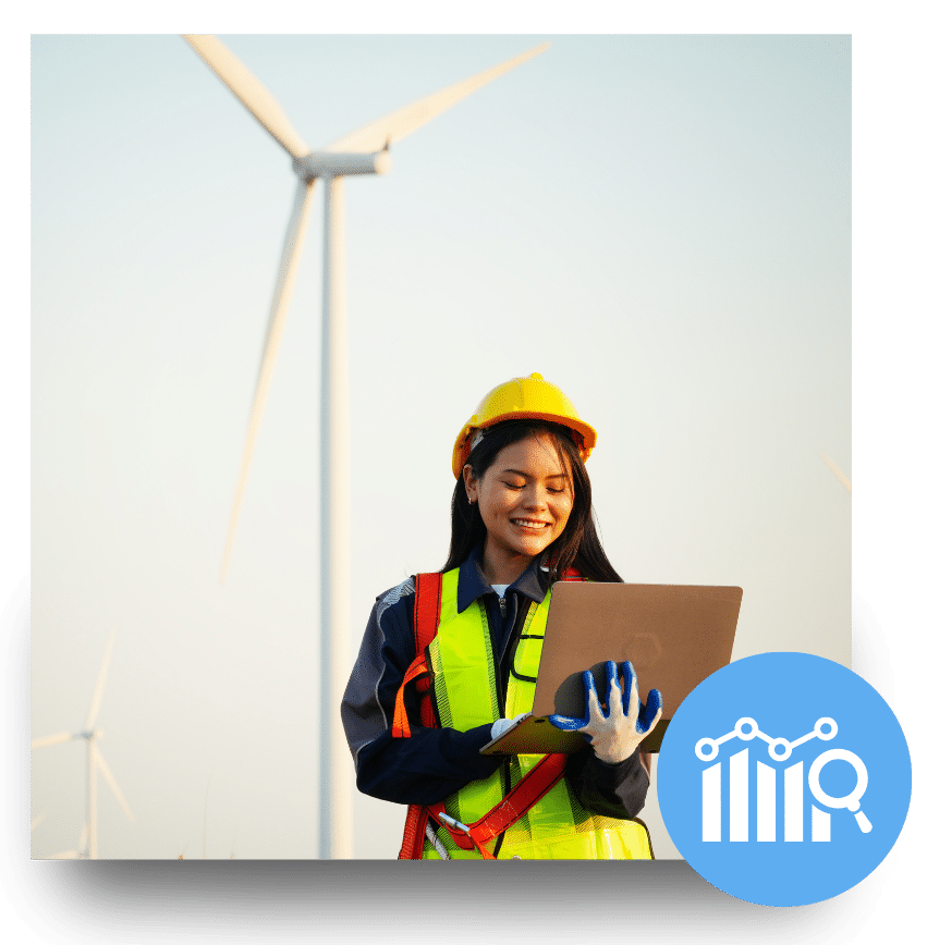 Female engineer with laptop and safety gear standing in a wind farm, representing women in renewable energy.
