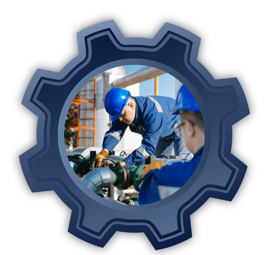 Two industrial workers in blue uniforms and hard hats inspect and repair green pipes on a factory site.